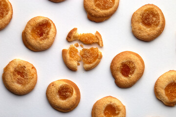 Nine handmade cookies with apricot jam arranged in even rows from an angle. One in the center is broken. on white background