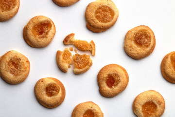 Ten handmade cookies with apricot jam arranged in even rows from an angle. One in the center is broken. on white background