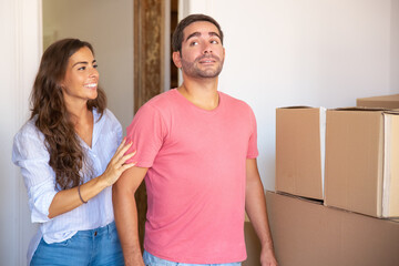 Happy excited family couple standing among carton boxes, looking over their new apartment. Medium shot. New home concept