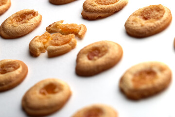 eleven handmade cookies with apricot jam arranged in even rows from an angle. One in the center is broken. on white background
