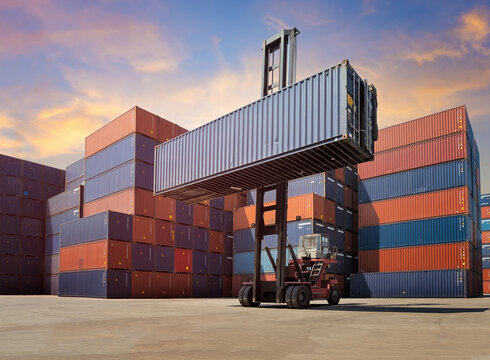 Forklift truck lifting Cargo containers in shipping yard for import,export industrial against sunrise sky environment.