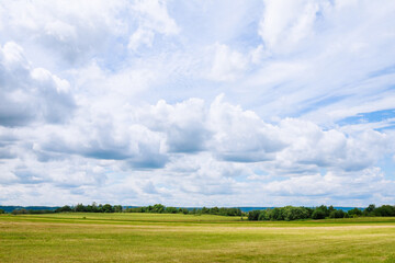 Fototapeta premium White clouds against a blue sky over a grassy field.