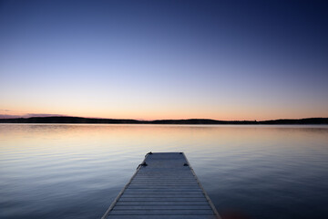 Obraz premium Small boat pier in cottage country. Calm lake with clear sky.