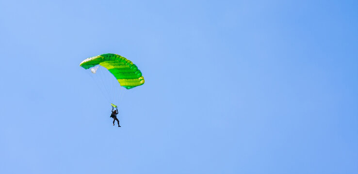 A parachutist with a light green parachute canopy against a background of blue sky and white clouds. Skydiving.