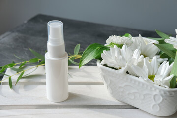 unbranded white bottle of cosmetic product. collagen solution for face care. white flowers in a vase. copy space for text. anti age cosmetic serum. 