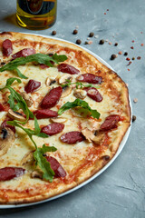 Italian pizza with with smoked sausages, mushrooms, arugula on a gray background. Selective focus, food flat lay. Vertical