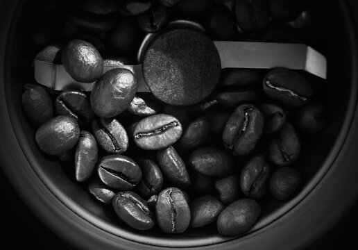 Black-and-white image of roasted coffee beans that are in the coffee grinder, and soon they will become ground coffee. The view from the top.