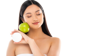 Obraz na płótnie Canvas young asian woman with closed eyes holding green apple and cosmetic cream near face isolated on white