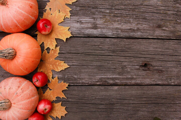 Naklejka na ściany i meble Orange pumpkins, red apples, yellow maple leaves on rough rustic wooden table background. Top view, copy space. Food, holiday, thanksgiving, harvest season concept.