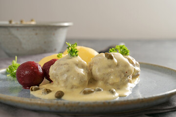 Boiled meatballs in white sauce with capers, in Germany called Koenigsberger Klopse, with beetroot, potatoes and parsley garnish on a gray plate, copy space, close-up with selected focus