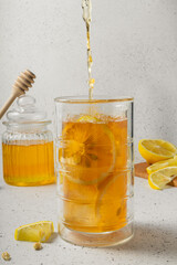 selective focus, a tall glass of lemon iced tea with a jar of honey on a light background