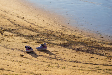 Fototapeta na wymiar Pair of chabby sneakers on a beach near water