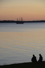 Old sail ship passes out on the sea while two persons in silhouette watch