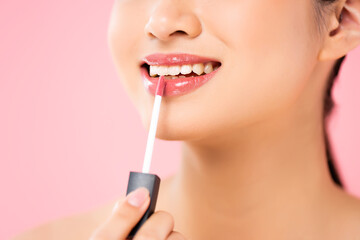 cropped view of young woman applying lip gloss isolated on pink