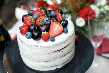 Delicious festive naked cake with butter cream. The cake is decorated with fresh blueberries, cherries and strawberries. Top view. A light cake for a birthday or wedding.