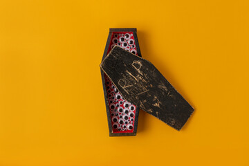 A yellow Halloween background with a miniature homemade red and black coffin with a lot of plastic eyes peeking out.