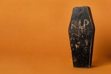 Toy homemade wooden black coffin on an orange background. Festive halloween composition with copy space.