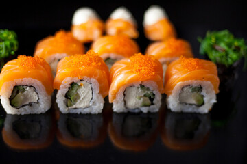Salmon sushi set. Sushi roll Philadelphia with red fish, salmon, red caviar. Roll with soft avocado and cream cheese under a layer of massago caviar. Classic sushi on a black background. Food.