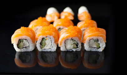 Salmon sushi set. Sushi roll Philadelphia with red fish, salmon, red caviar. Roll with soft avocado and cream cheese under a layer of massago caviar. Classic sushi on a black background. Food.