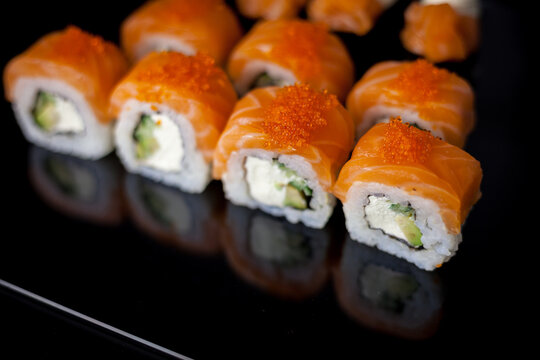 Salmon sushi set. Sushi roll Philadelphia with red fish, salmon, red caviar. Roll with soft avocado and cream cheese under a layer of massago caviar. Classic sushi on a black background. Food.