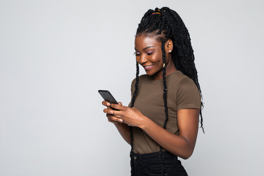 Happy young african woman casually dressed holding mobile phone standing isolated over gray background