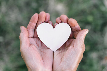 Fototapeta premium Grandma's hand holds a heart. The concept of protecting the elderly, retirement