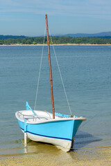 wooden blue fishing sailboat anchored near the shore