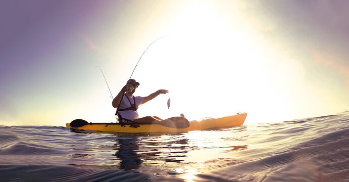 Fisherman standing on a kayak catch a fish against sunset.