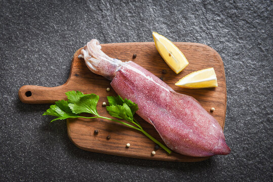Raw squid on wooden cutting board with lemon parsley on the dark plate seafood market - fresh squids octopus or cuttlefish for cooked food salad restaurant