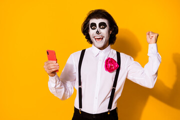 Portrait of his he nice handsome spooky cheerful cheery glad guy using device gadget fast speed celebrating good news luck app 5g calavera isolated bright vivid shine vibrant yellow color background
