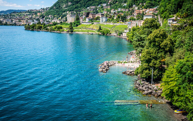 Top view of Lake Geneva shoreline in Veytaux with people swimming and Montreux city in background in Switzerland