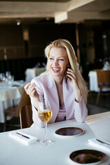 Beautiful businesswoman dressed in the suit drinking wine. Businesswoman talking to the phone in the restaurant