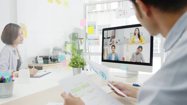Asia businesspeople using desktop talk to colleagues discussing business brainstorm about plan in video call meeting in new normal office. Lifestyle social distancing and work after corona virus.