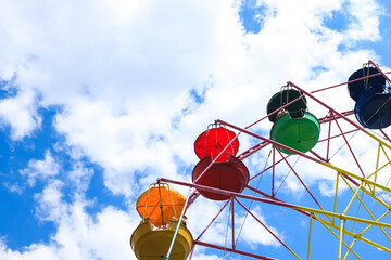 Vintage old fashioned bright multicolored Ferris wheel against a blue cloudy sky. Copy space.