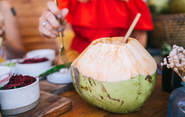 Coconut milk drink in shell on table with anonymous woman