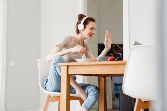 Image of cheerful girl working with laptop while having breakfast