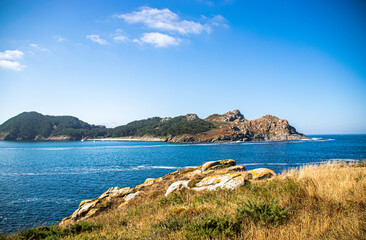 Obraz premium Photo of some rocks and a lighthouse in Galicia, Spain during summer holidays. Blue ocean, empty beach.