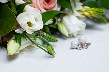 
Wedding accessories. Pearl earrings with diamonds next to white roses from the bride's bouquet on a light background.