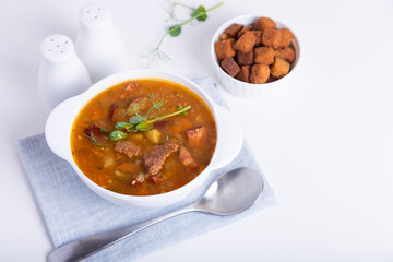 Pea soup with meat, smoked sausage, pea sprouts and croutons. Traditional Russian dish. Home kitchen. Close-up, selective focus.