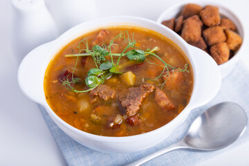 Pea soup with meat, smoked sausage, pea sprouts and croutons. Traditional Russian dish. Home kitchen. Close-up, selective focus.