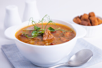 Pea soup with meat, smoked sausage, pea sprouts and croutons. Traditional Russian dish. Home kitchen. Close-up, selective focus.