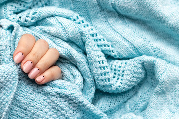 Female hand in a blue knitted sweater fabric with trendy beautiful manicure - pink nude nails with black small dots with copy space. Selective focus