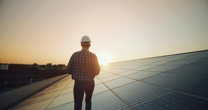 An young engineer is checking with tablet an operation of sun and cleanliness on field of photovoltaic solar panels on a sunset. 