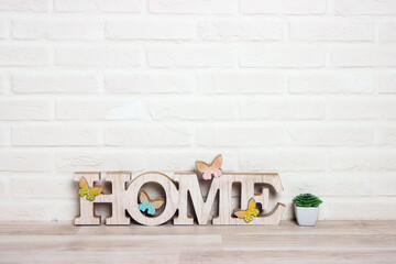The word HOME with a houseplant on the floor against a white brick wall background.