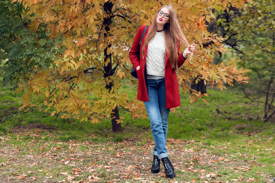 Full height autumn fashion image of pretty nice woman in red stylish coat and knitted hat, red lips posing on yellow park.