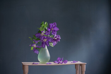 clematis flowers in glass vase  on vintage wooden shelf