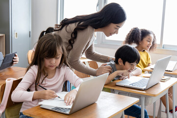 An Asian female teacher teaches primary school students to use computers and tablets to search for knowledge and information through the Internet. Classroom diversity students. Back to school concept