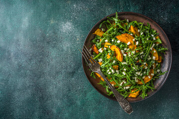 Homemade pumpkin salad with grilled pumpkin slices, arugula and cheese. Autumn pumpkin salad recipe, dark background copy space