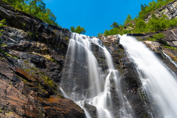 Fototapeta premium Skjervsfossen waterfall, on the road between Granvin and Voss, Hordaland, Norway. Impressive beautiful win falls plunging 150 metres in a narrow canyon