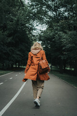 A girl in an orange raincoat walks with her back on the road in the park